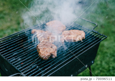 Steaks are fried on a metal grill in smoke. 70096511