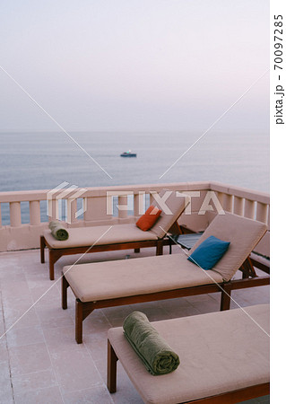 Wooden loungers near the pool at the villa by the sea, at sunset. Wooden loungers near the pool at the villa by the sea, at sunset. 70097285