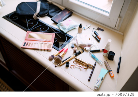 Makeup artist set. Eyeshadow palette, makeup brushes, mascara and eyelash curler on the windowsill by the window. 70097329