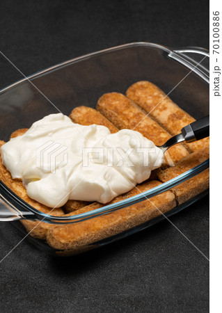 tiramisu dessert cooking - Traditional Italian Savoiardi ladyfingers Biscuits and cream in glass baking dish on dark concrete background 70100886