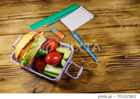 Back to school concept. School supplies and lunch box with burgers and fresh vegetables on a wooden table 70102862