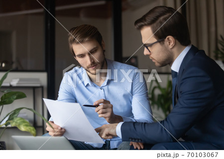 Focused young employee discussing paper document with executive manager. 70103067