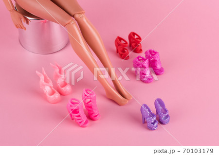 Doll with long skinny legs and stylish shoes on pink background. Plastic doll trying on high heels shoes. Woman choosing new shoes, deciding which pair to buy. Fashion and shopping concept. 70103179