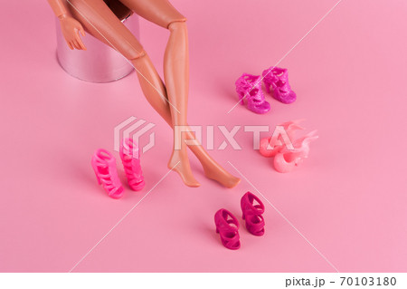 Doll with long skinny legs and stylish shoes on pink background. Plastic doll trying on high heels shoes. Woman choosing new shoes, deciding which pair to buy. Fashion and shopping concept. 70103180