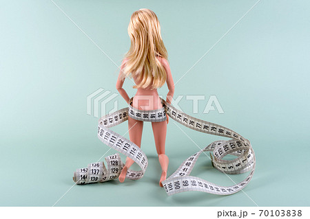 Doll wrapped in measuring tape. Tied up fashion doll, weight loss concept. Fasting, weightloss and slimming. Diet, anorexia, eating disorder, overeating control, female fight for perfect fit body. 70103838