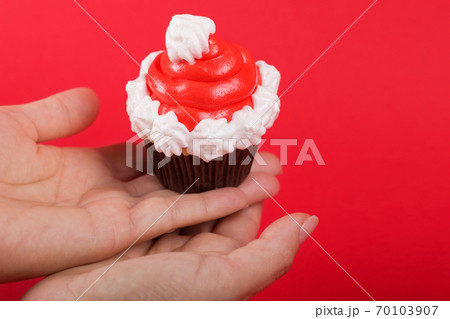 female hands holding cupcake in the shape of red santa claus hat, holiday concept 70103907