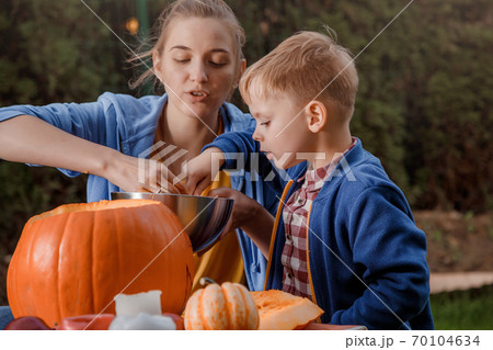A boy and his mother cut a pumpkin. A young mother and son are preparing a pumpkin for Halloween. Preparing for Halloween. Peel an orange pumpkin. A boy and his mother cut a pumpkin. A young mother and son are preparing a pumpkin for Halloween. Preparing for Halloween. Peel an orange pumpkin. 70104634