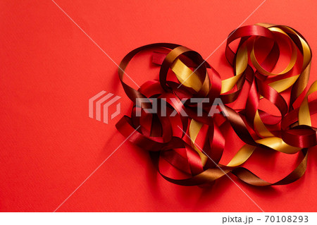 赤い無地の背景に赤 茶色 金色の絡んだリボンの写真素材