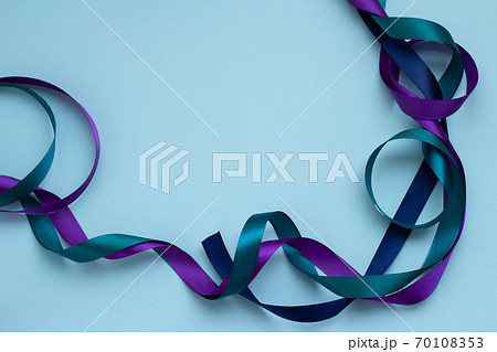 青い無地の背景に青 緑 紫の絡んだリボンの写真素材