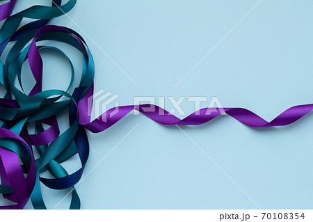 青い無地の背景に青 緑 紫の絡んだリボンの写真素材