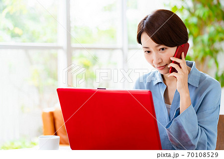 リビングでパソコンを使いながら電話をするミドル女性 70108529