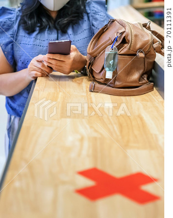 Mini alcohol gel bottle to kill Corona Virus(Covid-19) hang on a leather shoulder bag of a woman wearing a mask while use smartphone with alternative seating mark for social distancing in the mall. Mini alcohol gel bottle to kill Corona Virus(Covid-19) hang on a leather shoulder bag of a woman wearing a mask while use smartphone with alternative seating mark for social distancing in the mall. 70111391