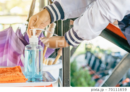 Hands of young woman pressed blue alcohol gel bottle to prevent the spreading of the Coronavirus (Covid-19) before entrance to cafeteria. Healthcare concept. New normal lifestyle. Selective focus 70111659