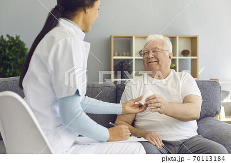 Young doctor visiting her senior patient at home, prescribing pills, supporting and cheering him up 70113184