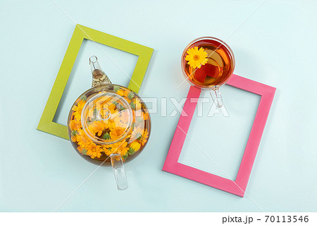 Cup of herbal tea and transparent teapot with calendula flowers on colors frame, blue background. Calendula Tea Benefits Your Health concept. Top view Flat lay 70113546