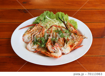 Grilled shrimp and cut in half with vegetables and cabbage  in white dish on the wooden table. 70113963