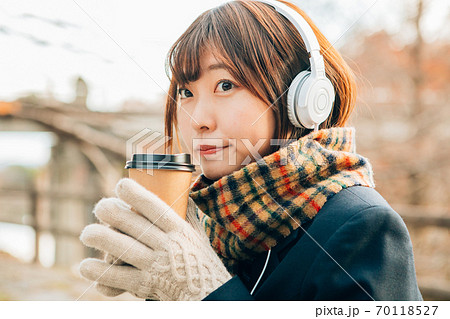 冬の屋外で音楽を聴きながらホットドリンク コーヒー を飲む女子高生の写真素材