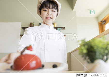 ケーキを出す女性カフェスタッフ　パティシエ 70118560