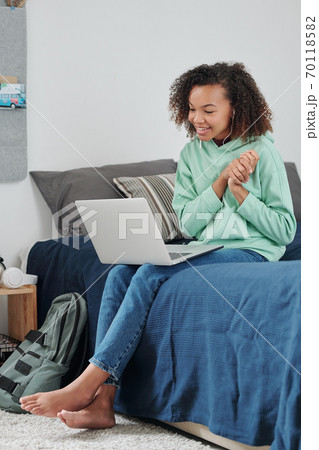 Contemporary cheerful mixed-race girl communicatng through video chat at home Contemporary cheerful mixed-race girl communicatng through video chat at home 70118582