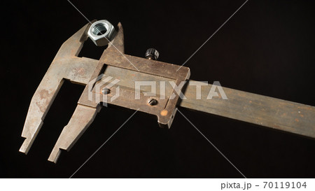 Old tools caliper with screw-nut in front of a black background Old tools caliper with screw-nut in front of a black background 70119104