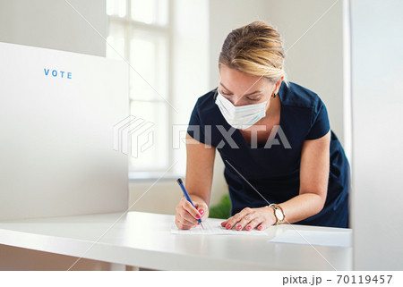 Portrait of woman voter with face mask in polling place, elections and coronavirus concept. Portrait of woman voter with face mask in polling place, elections and coronavirus concept. 70119457