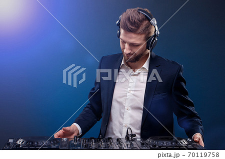Man DJ in dark suit play music on a Dj's mixer. Studio shot. Dark blue background 70119758