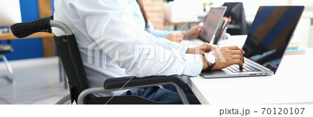 Disabled businessman sits in wheelchair in office and works at laptop Disabled businessman sits in wheelchair in office and works at laptop 70120107