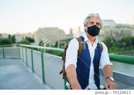 Mature man commuter with face mask and electric scooter outdoors in city, coronavirus concept. Mature man commuter with face mask and electric scooter outdoors in city, coronavirus concept. 70120611