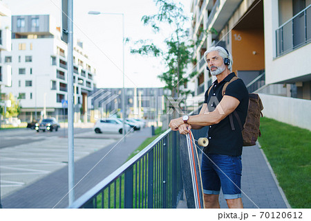 Portrait of mature man with skateboard outdoors in city, going back to work. 70120612
