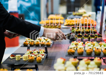 a man takes a canape with tongs from a tray during a coffee break a man takes a canape with tongs from a tray during a coffee break 70129683