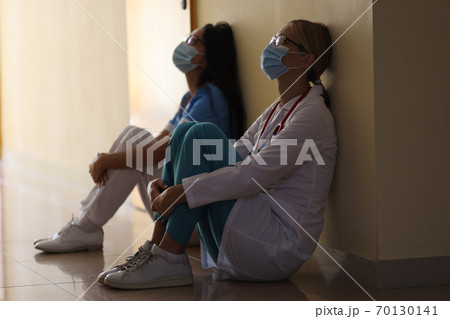 Young female doctor and nurse in medical masks sit in corridor of hospital Young female doctor and nurse in medical masks sit in corridor of hospital 70130141