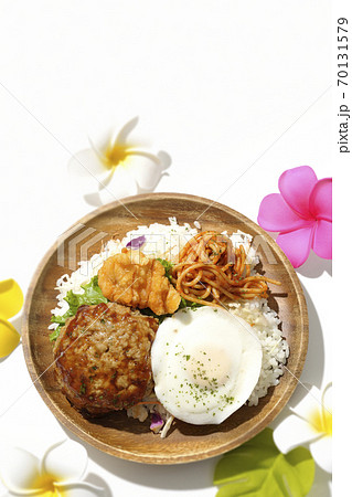 唐揚げやナポリタンも一緒に乗っているワンプレートのロコモコ丼とプルメリアの造花（白背景、俯瞰） 70131579