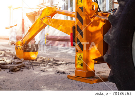An excavator's rear bucket digs in the courtyard of a residential building. Laying gas and water supply, replacing old pipes, accident 70136262