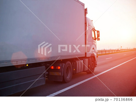 a truck with an isotherm semitrailer transports cargo along the highway against the backdrop of an evening sunset. Concept of delivery of goods, cargo transportation, copy space for text a truck with an isotherm semitrailer transports cargo along the highway against the backdrop of an evening sunset. Concept of delivery of goods, cargo transportation, copy space for text 70136866