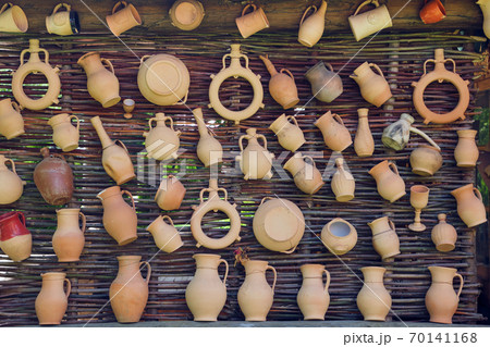 Rustic vintage clay jugs, pots and mugs hanging on wicker wall. Rustic vintage clay jugs, pots and mugs hanging on wicker wall. 70141168
