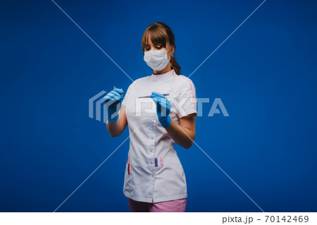 An attractive young female doctor holds a scalpel and looks directly at the camera. Concept of healthcare, treatment and surgery. Portrait of a medical practitioner on a blue background An attractive young female doctor holds a scalpel and looks directly at the camera. Concept of healthcare, treatment and surgery. Portrait of a medical practitioner on a blue background 70142469