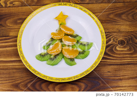 Christmas tree made of kiwi slices and mandarin lobules on wooden table. Top view. Creative idea for Christmas and New Year festive desserts. Funny food idea for kids 70142773