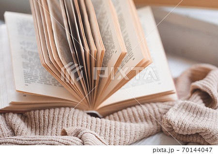 Warm and cosy hygge concept with white and beige sweater, opened book on a windowsill Warm and cosy hygge concept with white and beige sweater, opened book on a windowsill 70144047