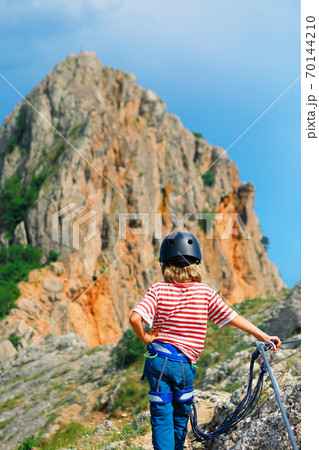 Child in hiking safety equipment stand under on mount top 70144210