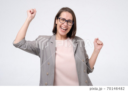 Mature caucasian woman in glasses doing a winner gesture raising fists up Mature caucasian woman in glasses doing a winner gesture raising fists up 70146482