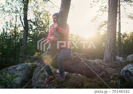 caucasian woman enjoying a summer evening outdoor hugging a tree. 70146582