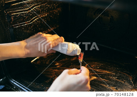 A tool for cleaning the oven and gas stoves. A woman cleans the oven from fat and pollution. 70148128