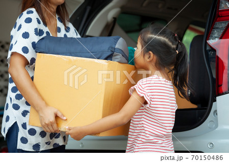 Happy asian child girl and mother helping to carry a cardboard box with stuffs moving into the car together to relocation on moving day. Home renovation and relocation concept. 70150486