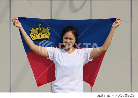 pretty lady is holding Liechtenstein flag in her hands and raising to the end of the arm at the back pretty lady is holding Liechtenstein flag in her hands and raising to the end of the arm at the back 70150925