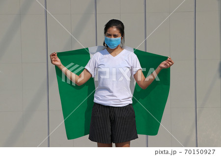 Masked woman prevent germs and holding Nigeria fabric flag on her shoulder Masked woman prevent germs and holding Nigeria fabric flag on her shoulder 70150927