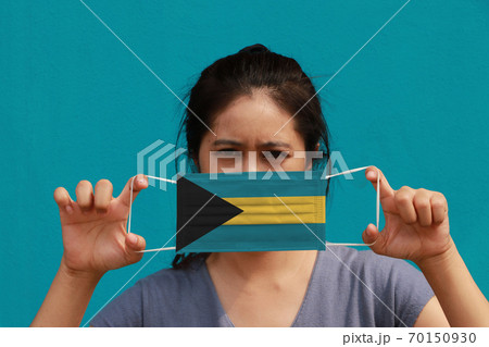 A woman with Bahamas flag on hygienic mask in her hand and lifted up the front face 70150930
