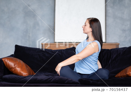 Young woman doing the spine twisting pose sitting at home on sofa. 70156437