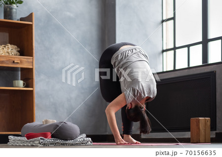 Woman working out indoors standing in Uttanasana during online lesson. Woman working out indoors standing in Uttanasana during online lesson. 70156635