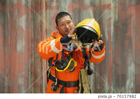 The portrait of Asian firefighters are wearing orange fire protection uniform mask and helmet front of building. The portrait of Asian firefighters are wearing orange fire protection uniform mask and helmet front of building. 70157982