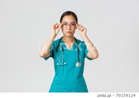 Covid-19, healthcare workers, pandemic concept. Confident serious-looking and determined asian female doctor, nurse in scrubs put on glasses, ready for shift in emergency room, white background Covid-19, healthcare workers, pandemic concept. Confident serious-looking and determined asian female doctor, nurse in scrubs put on glasses, ready for shift in emergency room, white background 70159124